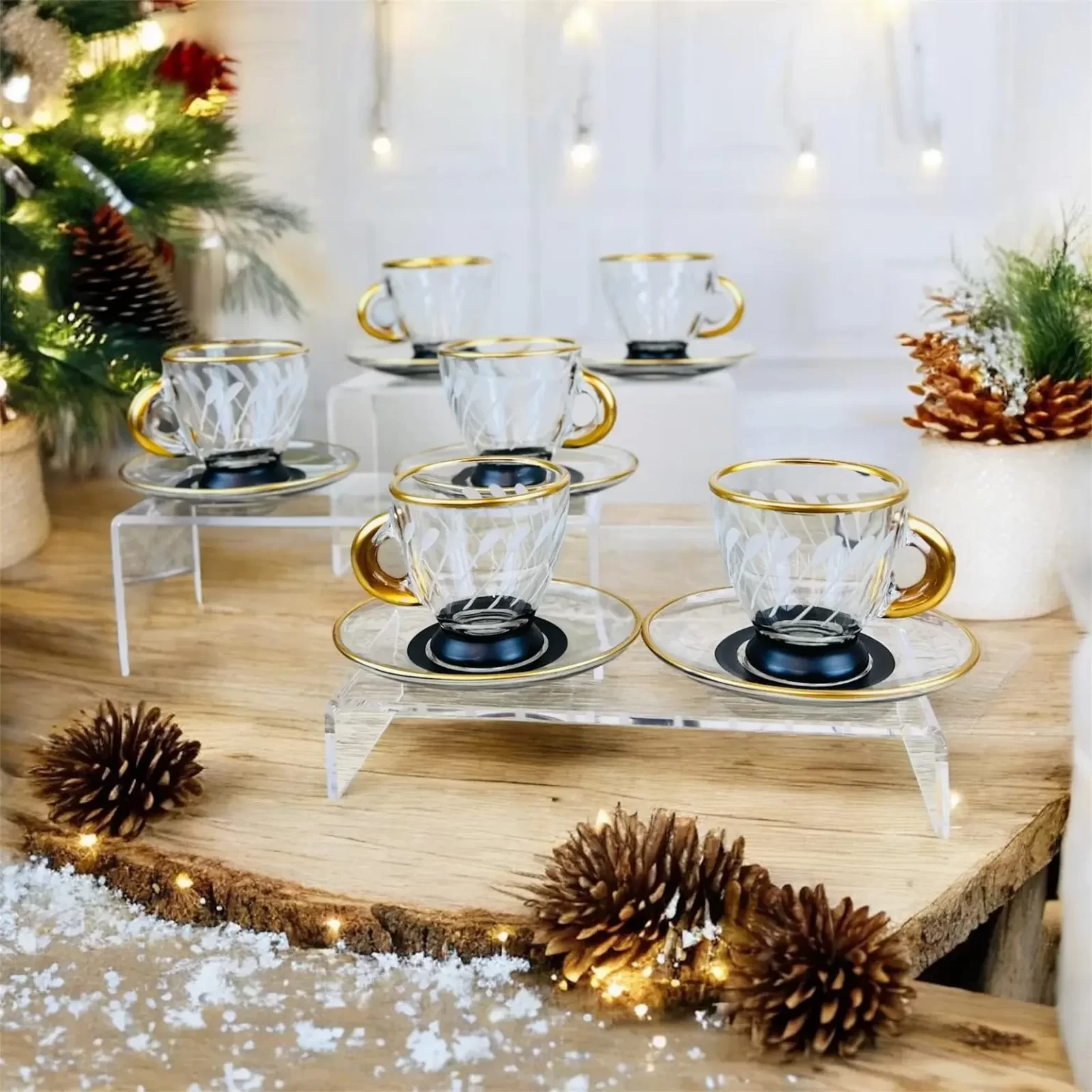 Elegant uppsättning av sex glaskoppar med guldkant och skålar, presenterade på träplatta med vinterprydnader och julbelysning i bakgrunden.