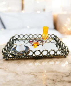 Rektangulært speilbrett med dekorativ metallkant, plassert på et marmorbord med en hvit kopp og et gult glass oppå.