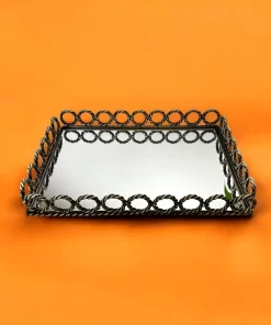 Rektangulært speilbrett med dekorativ metallkant i flettet design, plassert på en oransje bakgrunn.