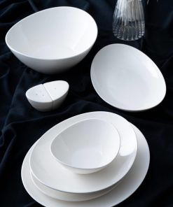 Hvitt porselensservise med boller, tallerkener og salt- og pepperbøsser på mørk duk.