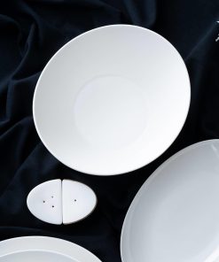 Hvitt servise og salt- og pepperbøsser arrangert på mørkt stoff.