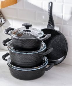 Sett med svarte gryter og stekepanne med glasslokk fra Acar, plassert på kjøkkenbenk med lys bakgrunn.