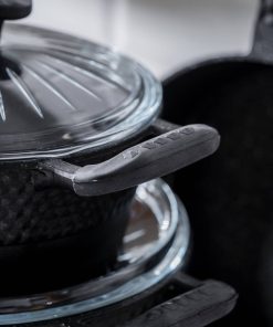 Nærbilde av svarte kjeler med glasslokk og håndtak med gummibelegg.